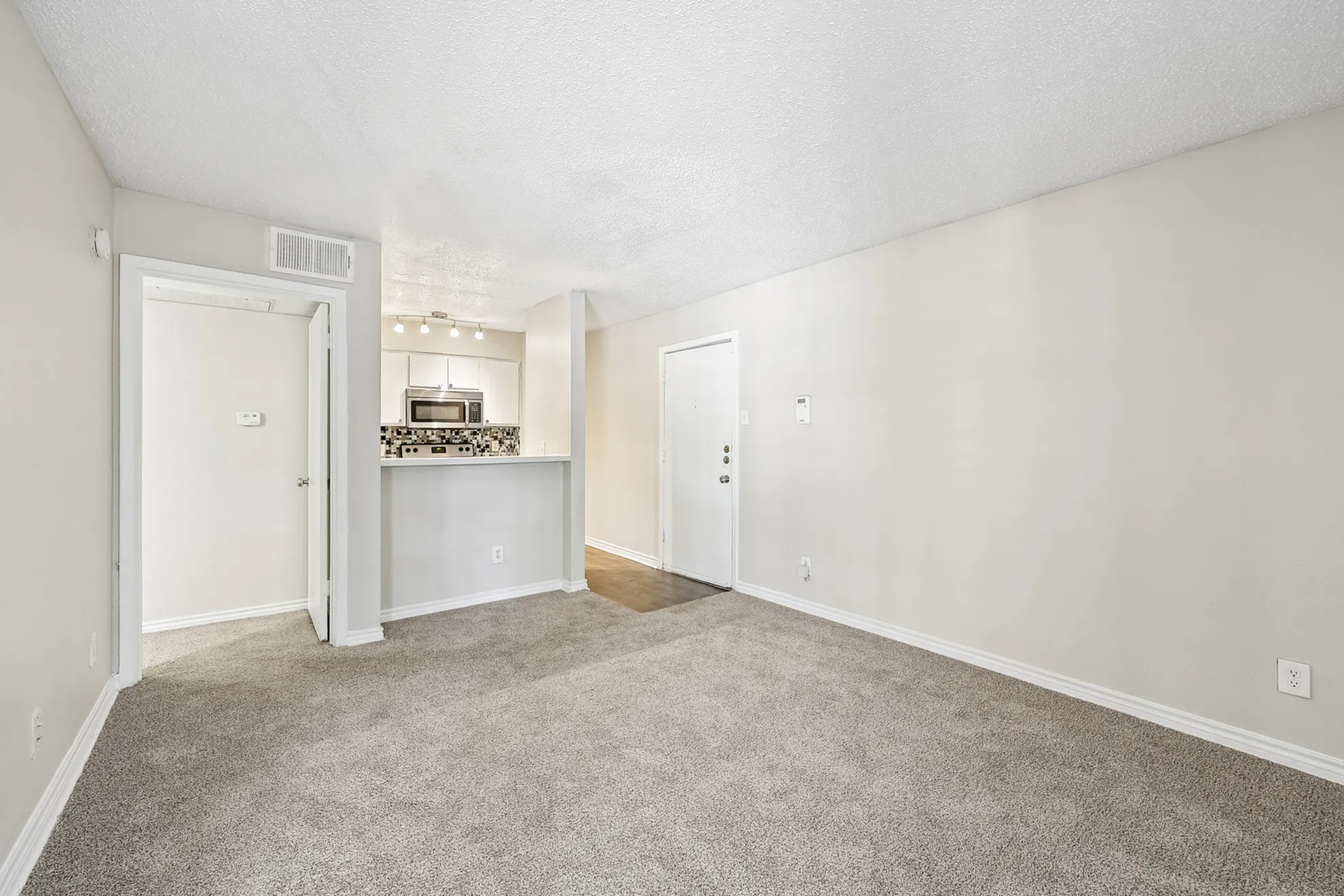 Bright and inviting living area with cozy carpet and open access to a modern kitchen featuring a sleek backsplash and stainless steel appliances.