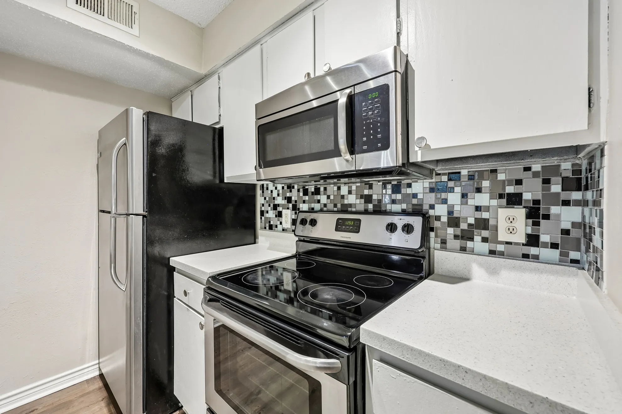 Modern kitchen with sleek stainless steel appliances, stylish mosaic backsplash, and white cabinetry.
