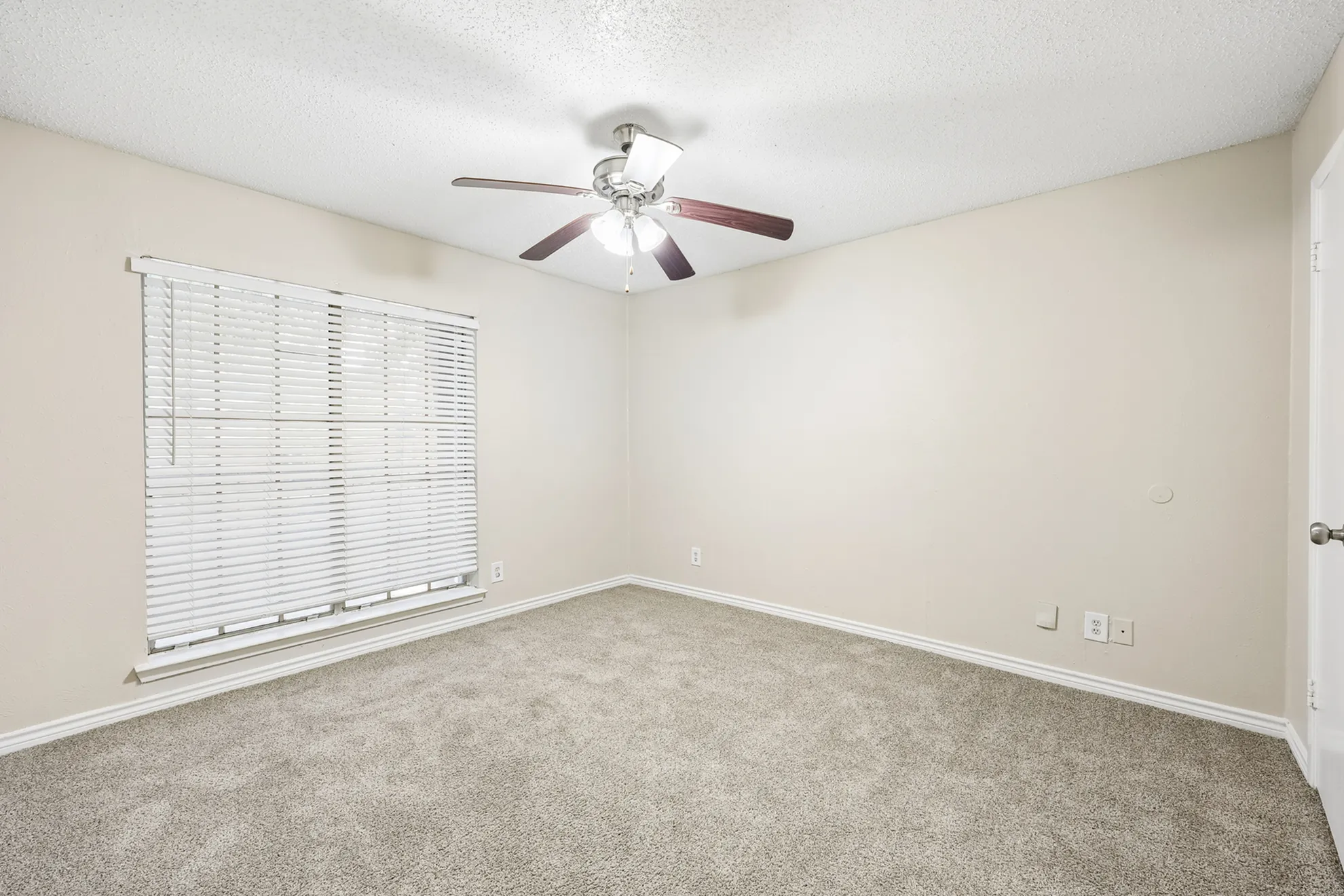 Bright and cozy bedroom with plush carpet, large window, and modern ceiling fan, perfect for relaxation.