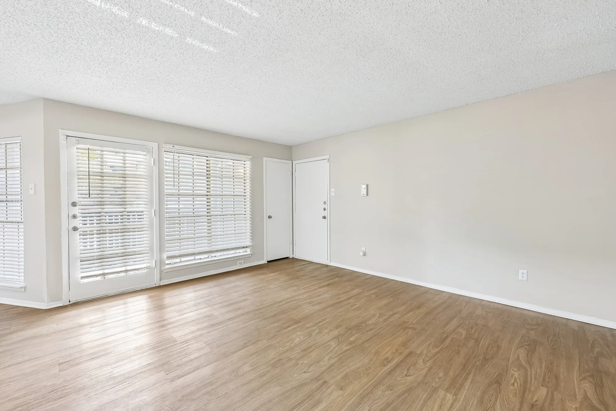Bright and airy living room featuring polished wood flooring and large windows with blinds, ideal for natural light.