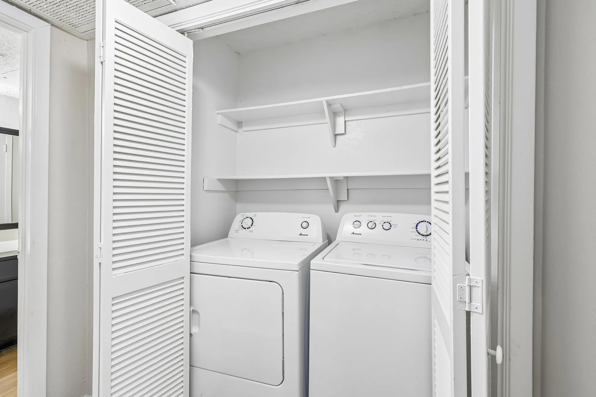 Convenient in-unit laundry area featuring a washer and dryer with ample shelving for storage.