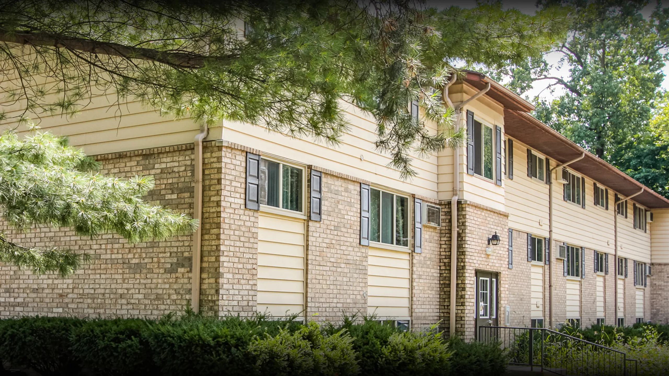 Charming two-story residential building with brick and siding exterior, surrounded by lush greenery, perfect for tranquil living.