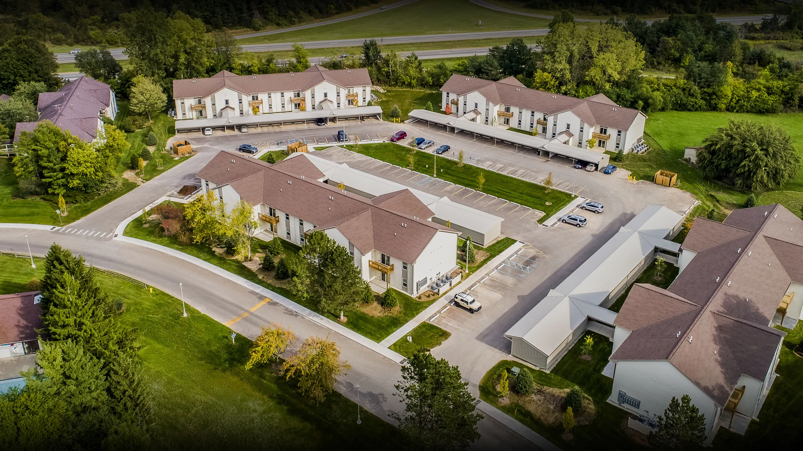 Inviting aerial view of a tranquil residential community surrounded by lush greenery and featuring well-maintained buildings and ample parking.