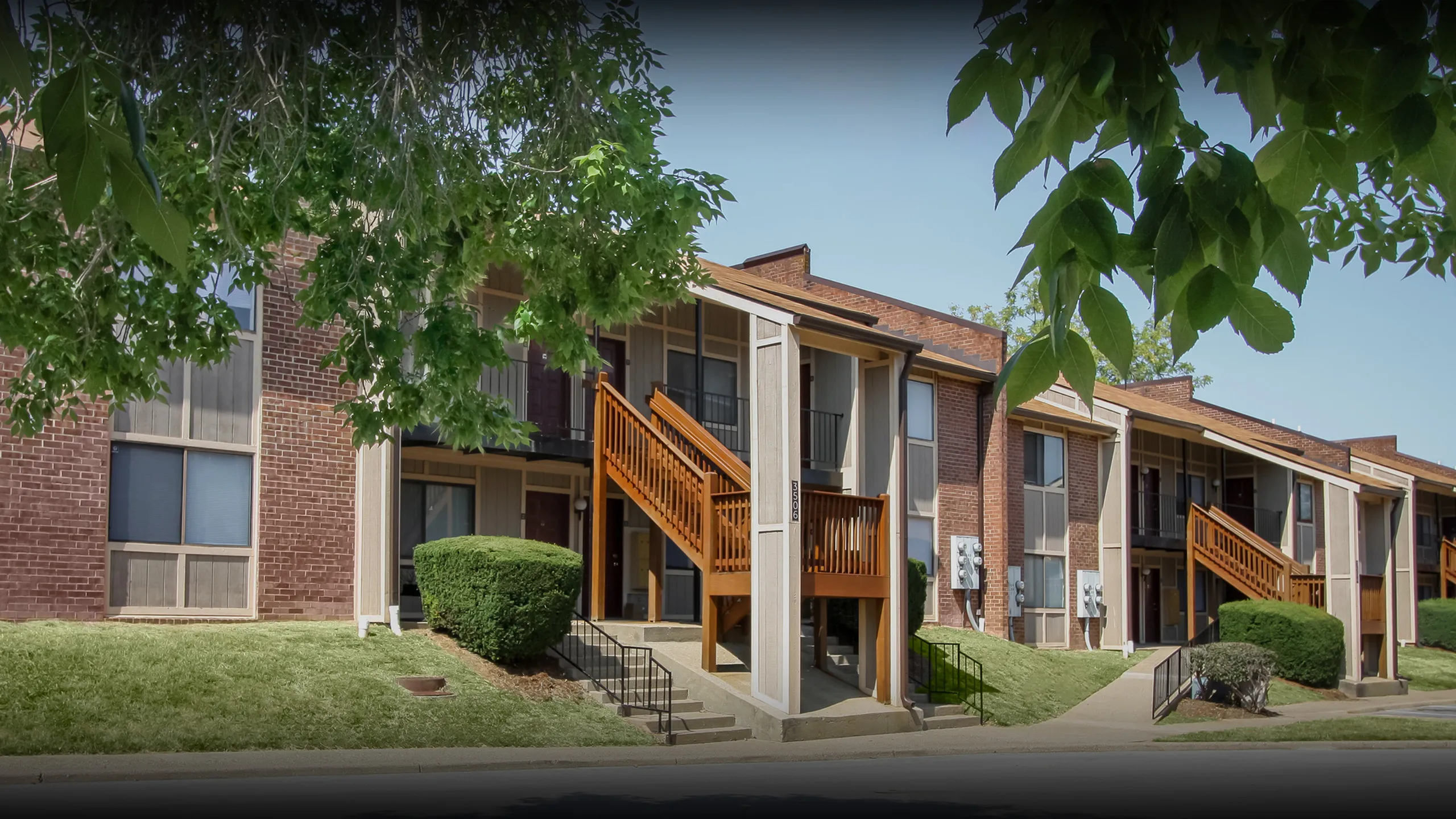 Beautiful suburban apartment complex showcasing red brick exteriors, wooden staircases, and lush green landscaping.