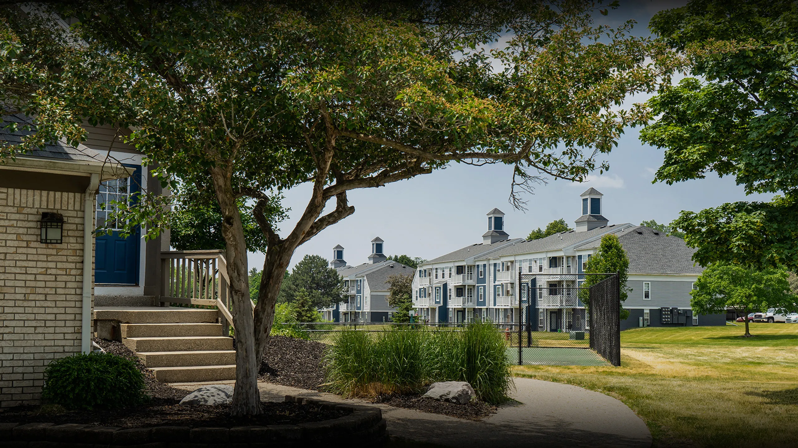 Charming apartment complex surrounded by lush greenery and a serene pathway, offering a warm and inviting atmosphere.