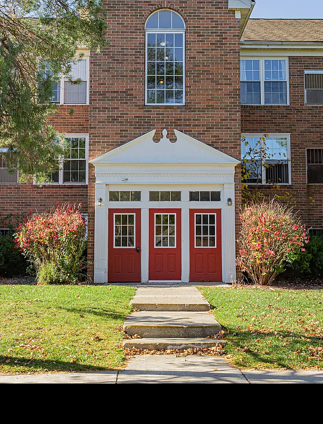 Charming brick apartment building with vibrant red doors and picturesque landscaping.