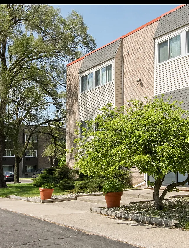 Charming apartment complex surrounded by lush greenery and mature trees, featuring a modern brick facade and large windows inviting natural light.