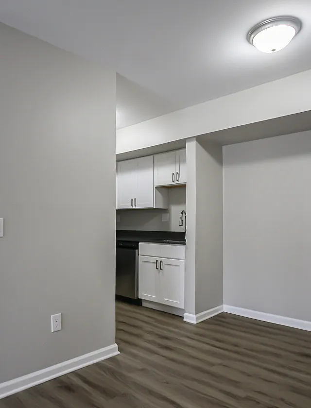 Modern apartment kitchen with sleek white cabinets, contemporary lighting, and elegant wood flooring.
