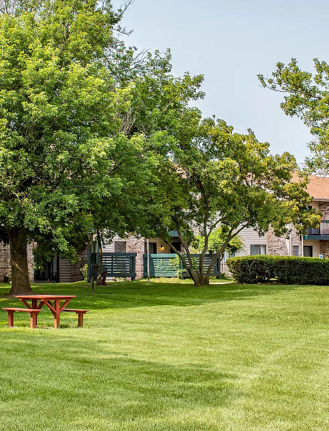 Inviting apartment exterior with lush greenery, mature trees, and a charming picnic area for outdoor relaxation.