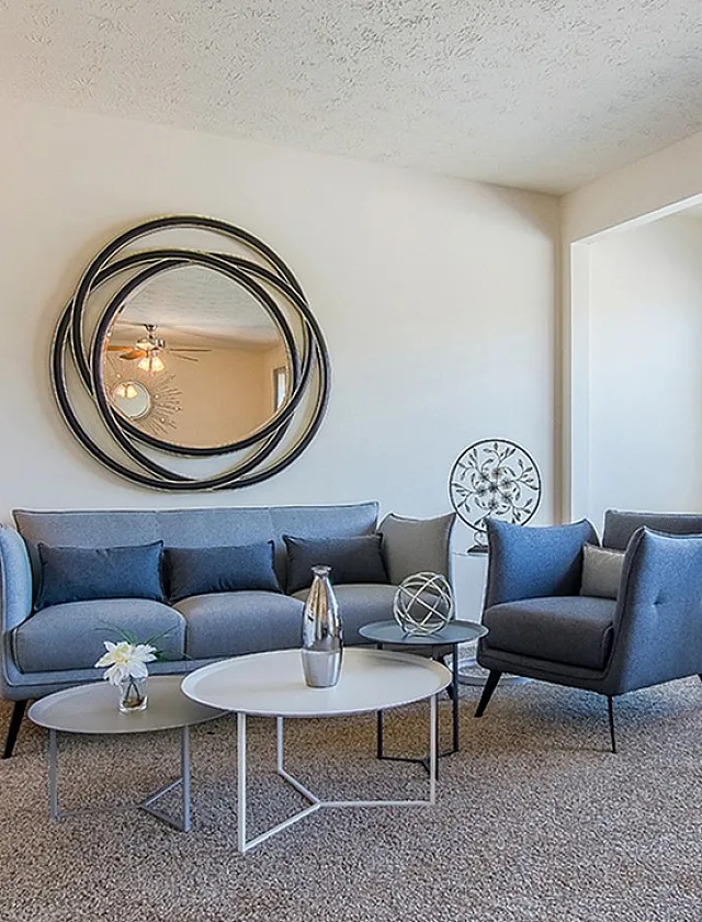 Modern living room with elegant blue sofa, chic round tables, and artistic mirror accents, creating a cozy and stylish atmosphere.