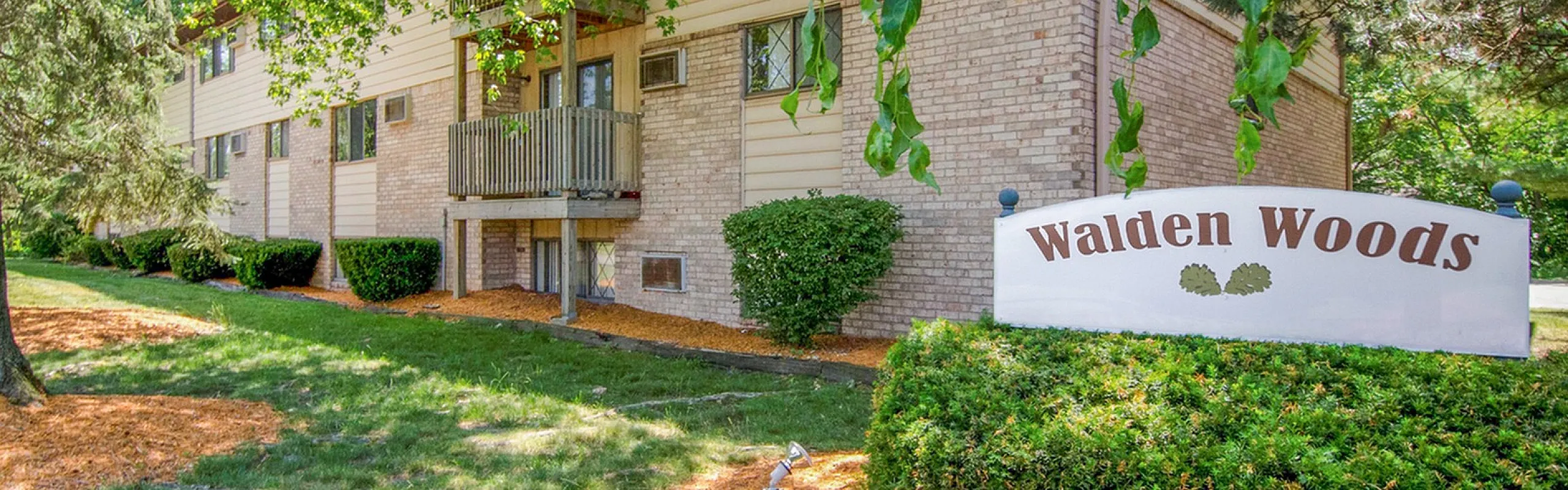 Charming brick apartment building surrounded by lush greenery at Walden Woods.