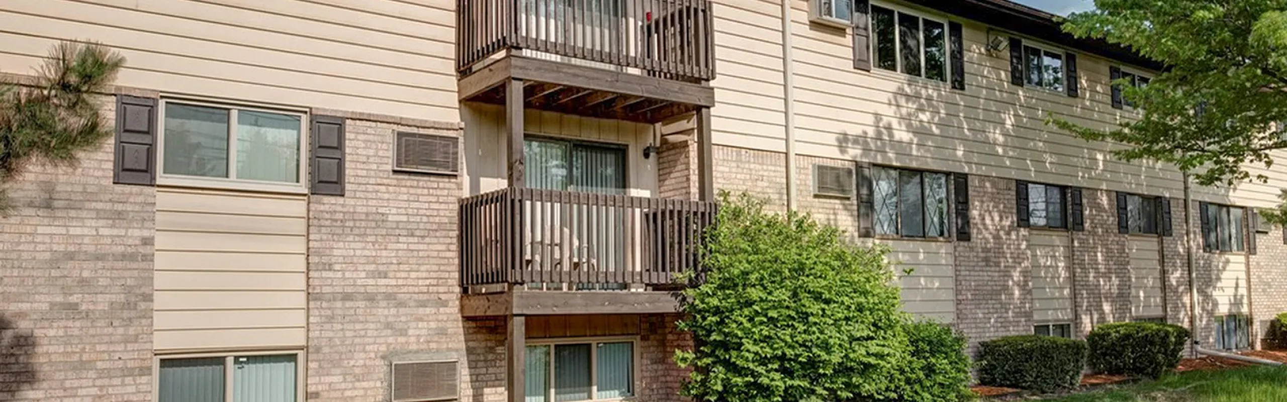 Charming apartment building with balconies, surrounded by lush greenery and blue skies, offering a serene living environment.