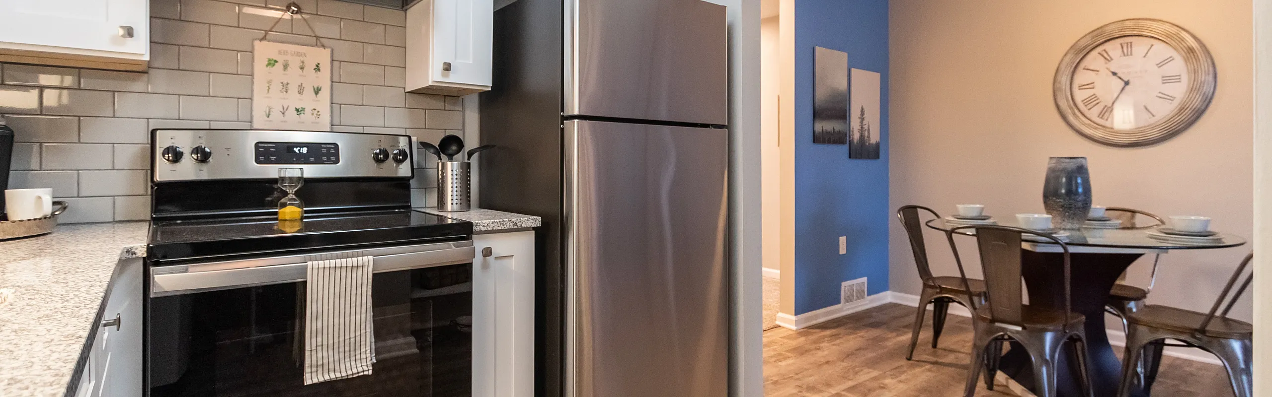 Bright modern kitchen with sleek stainless steel appliances, white cabinetry, and a cozy dining area featuring elegant decor and a charming wall clock.