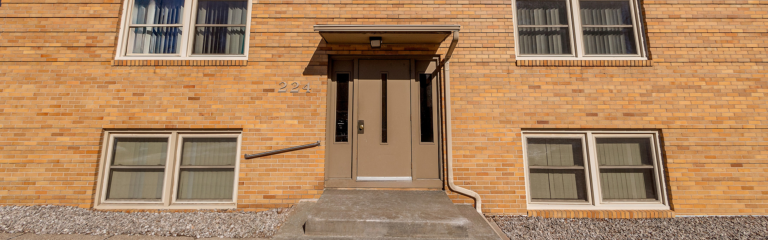 Charming brick apartment building with classic architecture, featuring multiple large windows and a welcoming entrance.