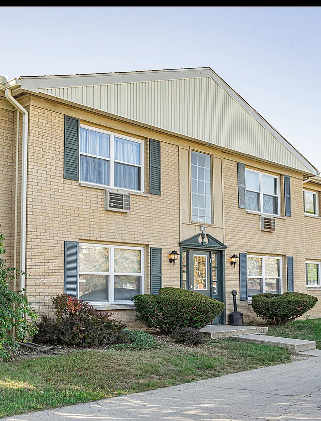 Charming brick apartment building with lush greenery and classic design, offering a welcoming entrance and well-maintained exterior.