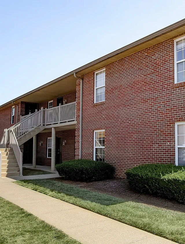 Charming brick apartment building with inviting balconies and well-maintained landscaping under a clear blue sky.