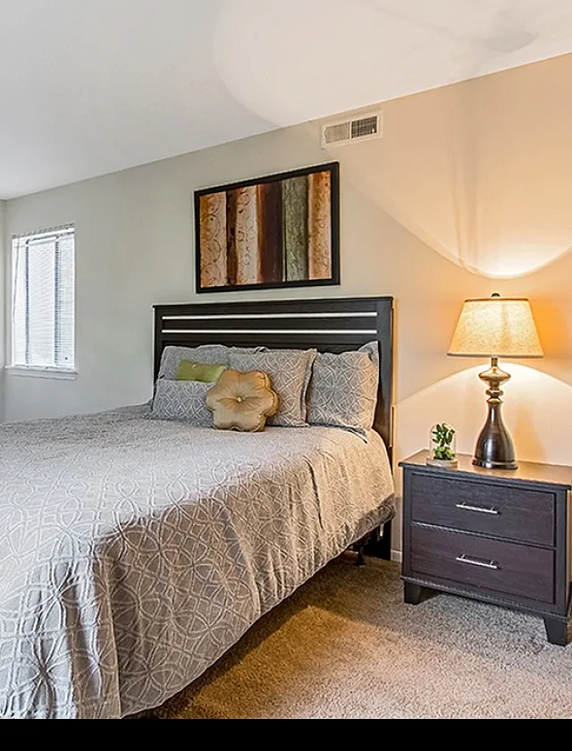 Cozy bedroom with elegant decor features a plush bed, stylish nightstand with lamp, and warm lighting for a tranquil retreat.
