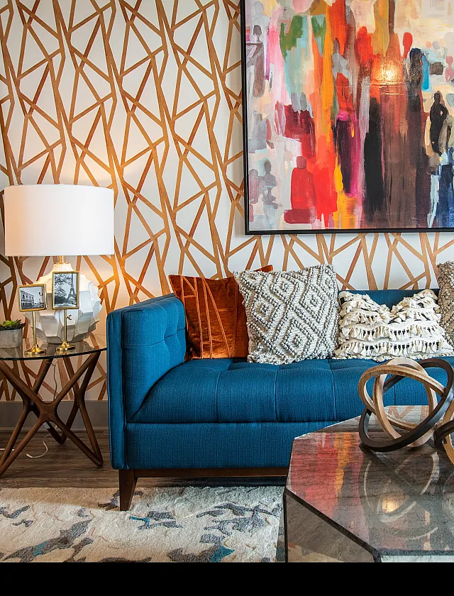 Chic living room featuring a vibrant abstract painting, patterned wallpaper, and a stylish blue sofa adorned with textured cushions.