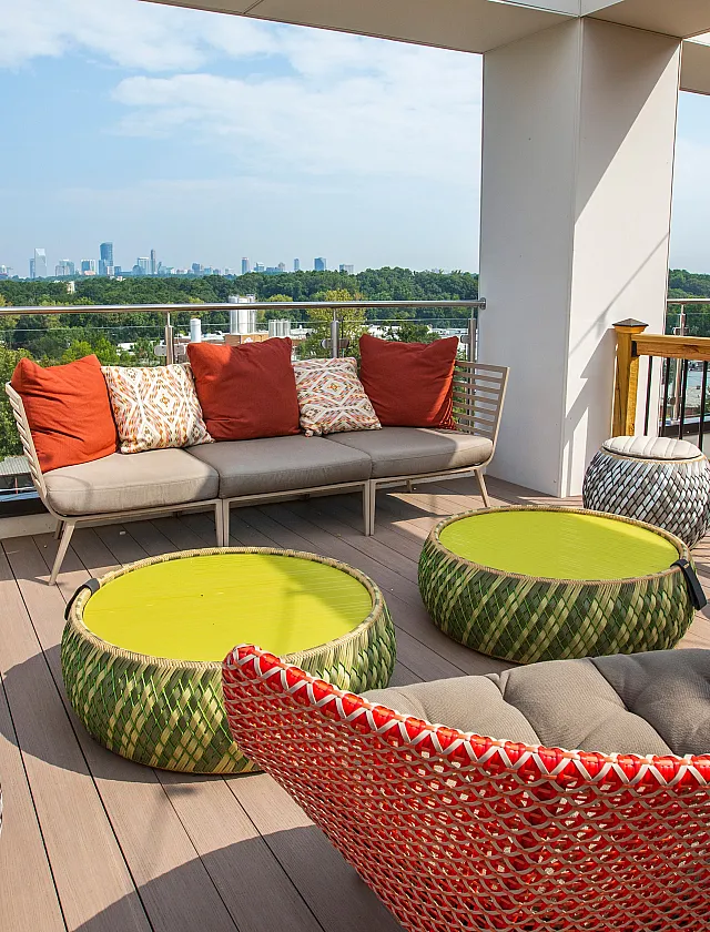 Chic rooftop terrace with vibrant wicker furniture, colorful cushions, and a stunning city skyline view.