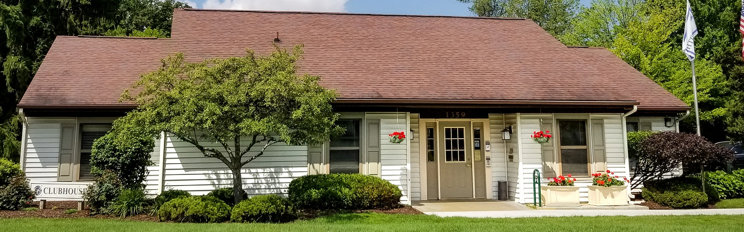 Charming clubhouse with a beautifully landscaped garden and vibrant flowers under a clear blue sky.