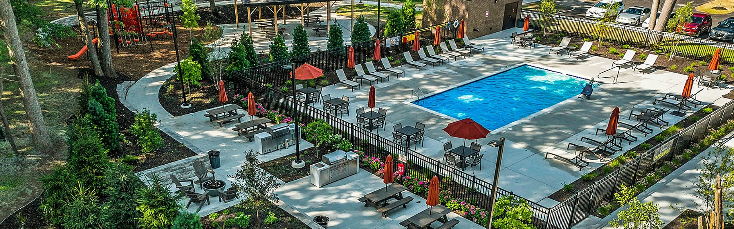 Luxurious outdoor area with sparkling pool, surrounded by sun loungers, lush greenery, and a cozy fire pit in a beautifully landscaped setting.
