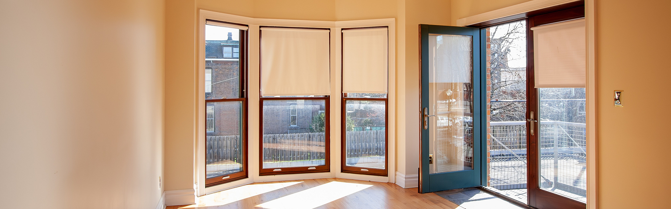 Sunlit room with beautiful hardwood floors, large bay windows, and a glass door leading to a spacious balcony.