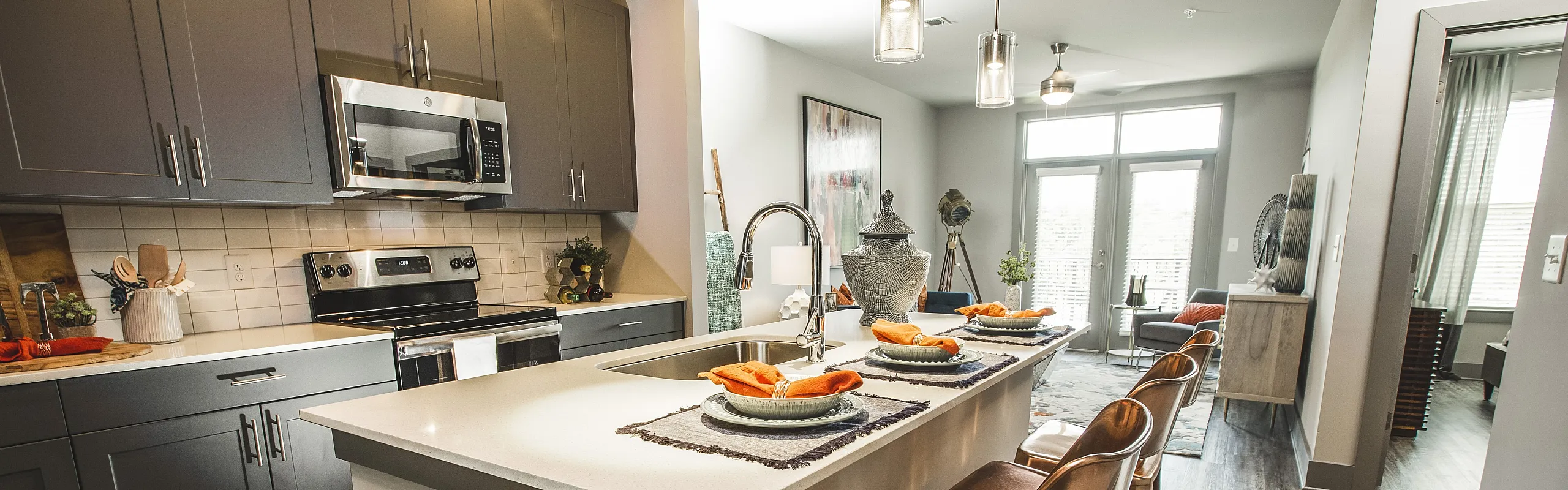 Contemporary kitchen and living space with sleek gray cabinetry, stainless steel appliances, and a stylish island with bar seating, perfect for modern living.