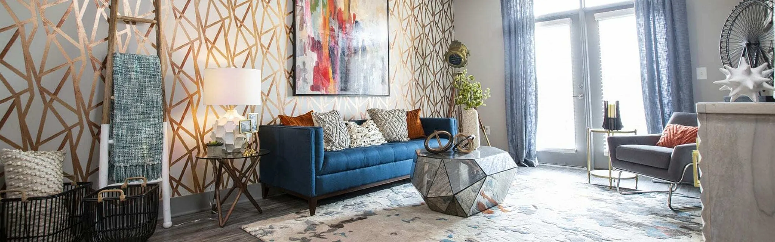 Chic living room with vibrant geometric accent wall, stylish blue sofa, modern artwork, and a unique mirrored coffee table under ample natural light.