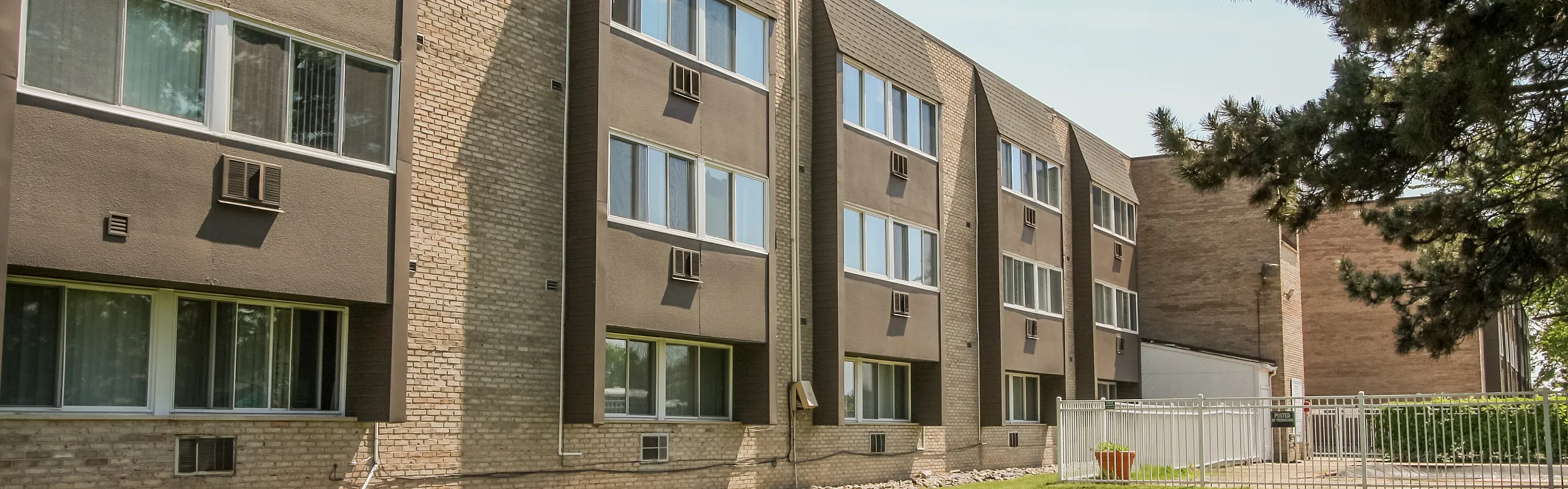 Charming apartment building with modern brick design, offering airy windows and lush green surroundings for a serene living experience.