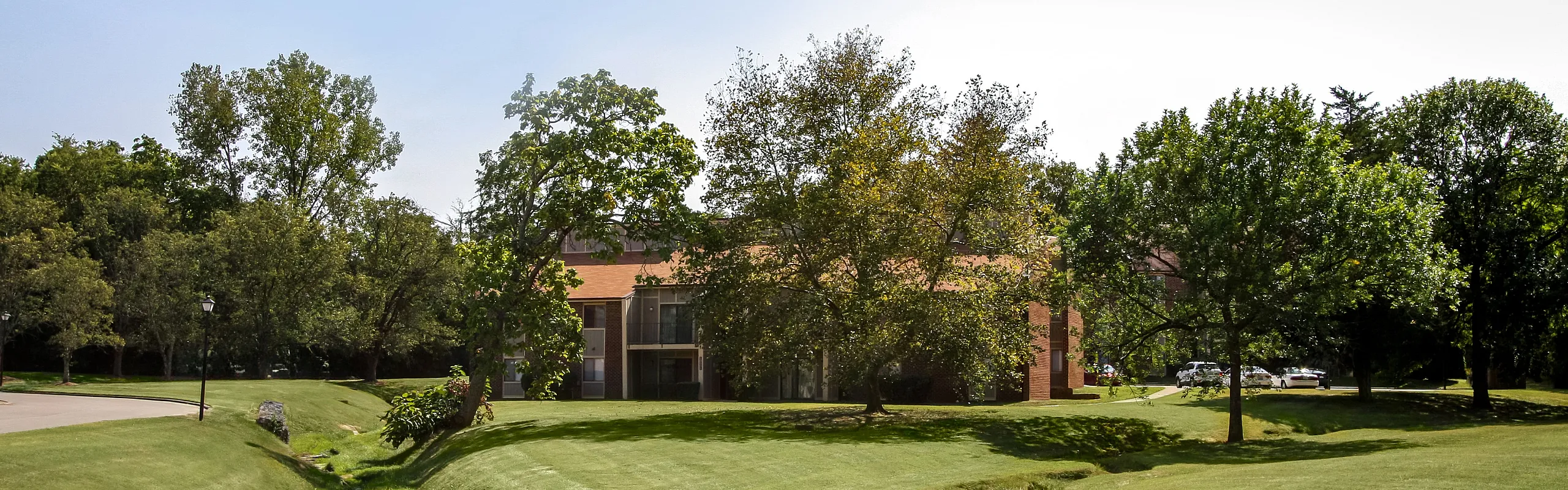 Charming apartment building nestled in lush green surroundings with a scenic creek and ample trees, offering serene and picturesque living.