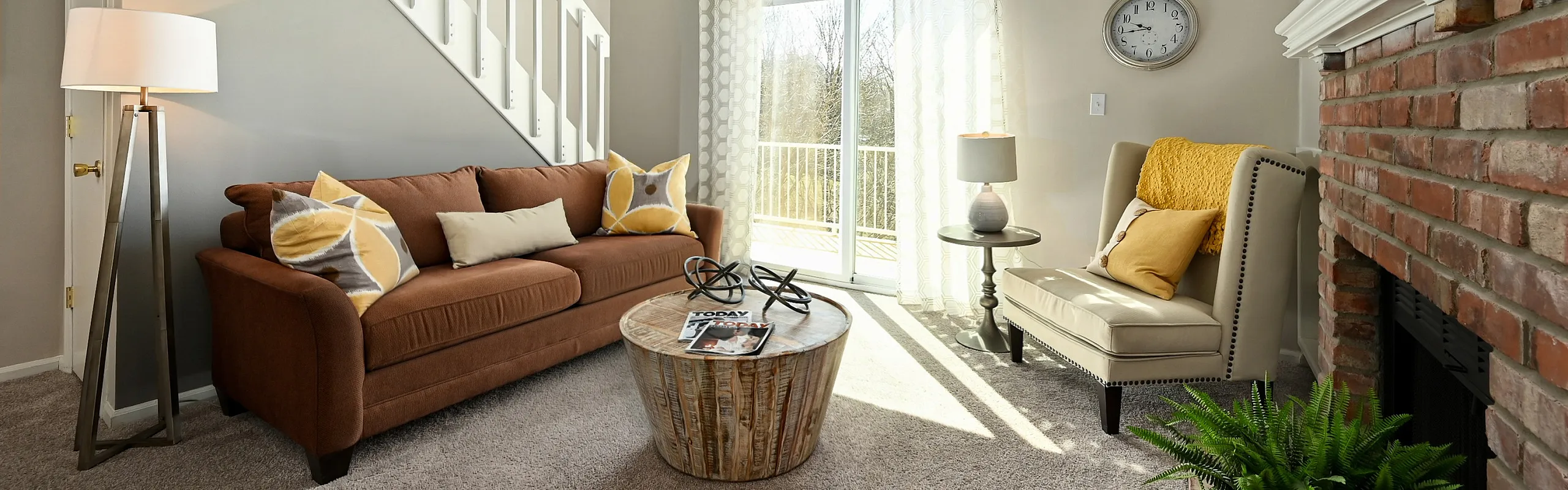 Charming living room with cozy brown sofa, elegant armchair by brick fireplace, and natural light from sliding glass doors.