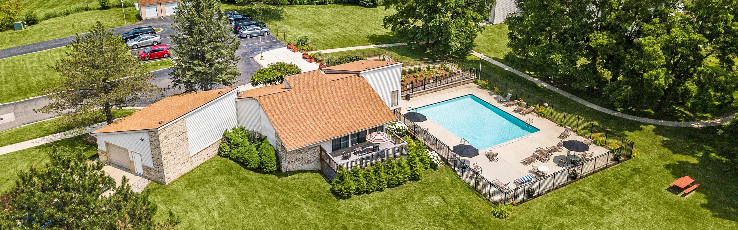 Charming residential area showcasing a lush green landscape, a stylish clubhouse, and a sparkling blue swimming pool surrounded by relaxing lounge chairs.