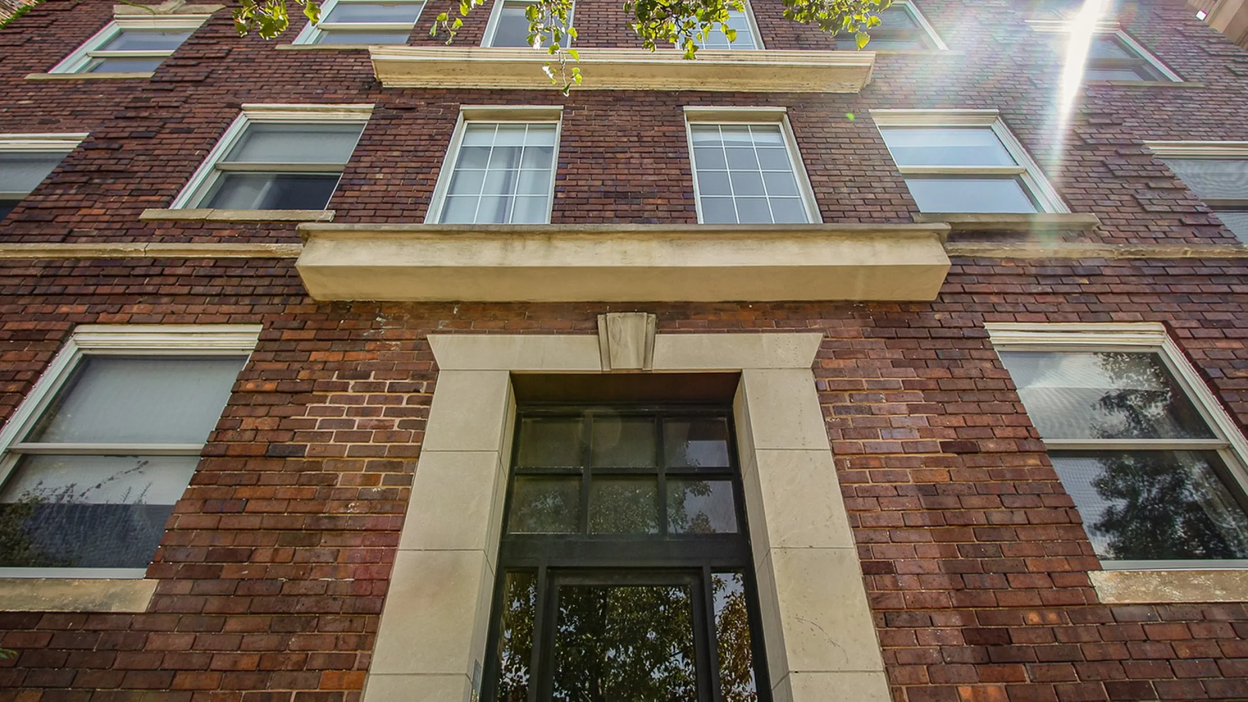 Charming brick apartment building facade with sunlit windows and decorative architectural details.
