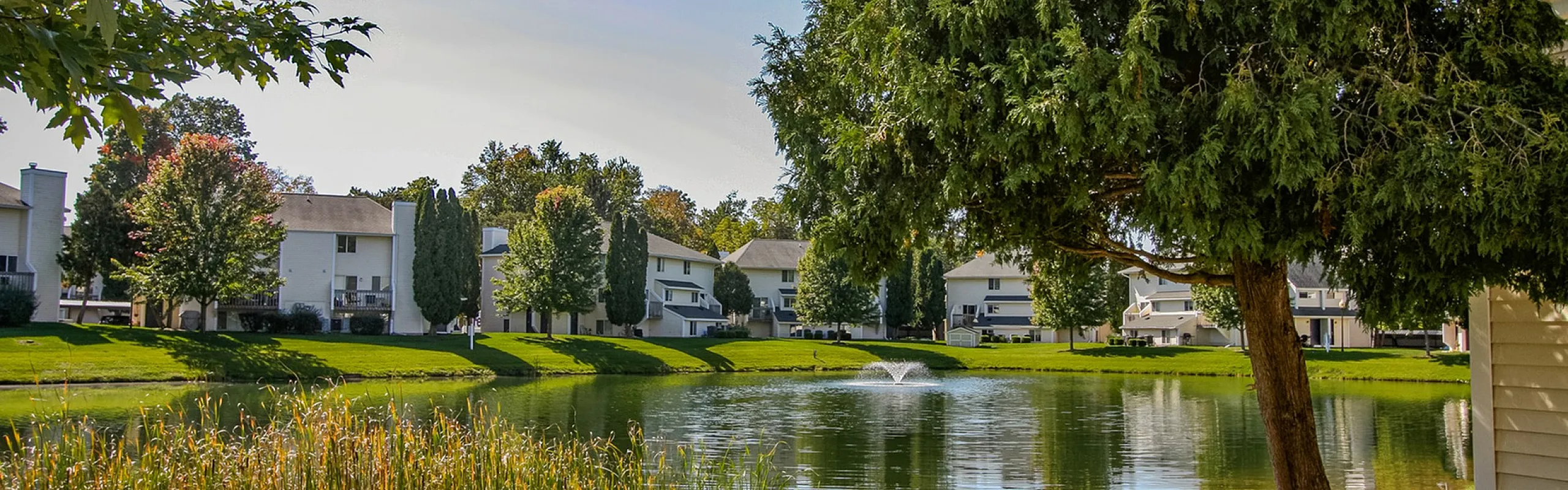 Serene apartment community with picturesque pond and lush greenery, perfect for tranquil living.