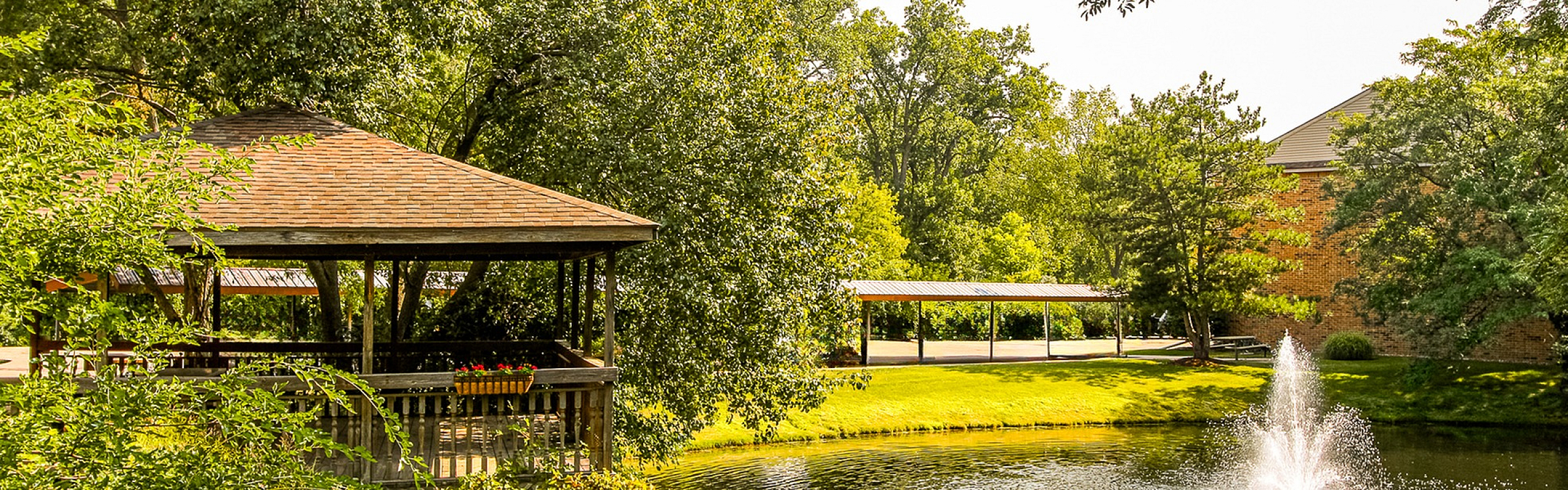 Tranquil outdoor setting featuring a charming gazebo by a serene pond, surrounded by lush greenery and a decorative fountain.
