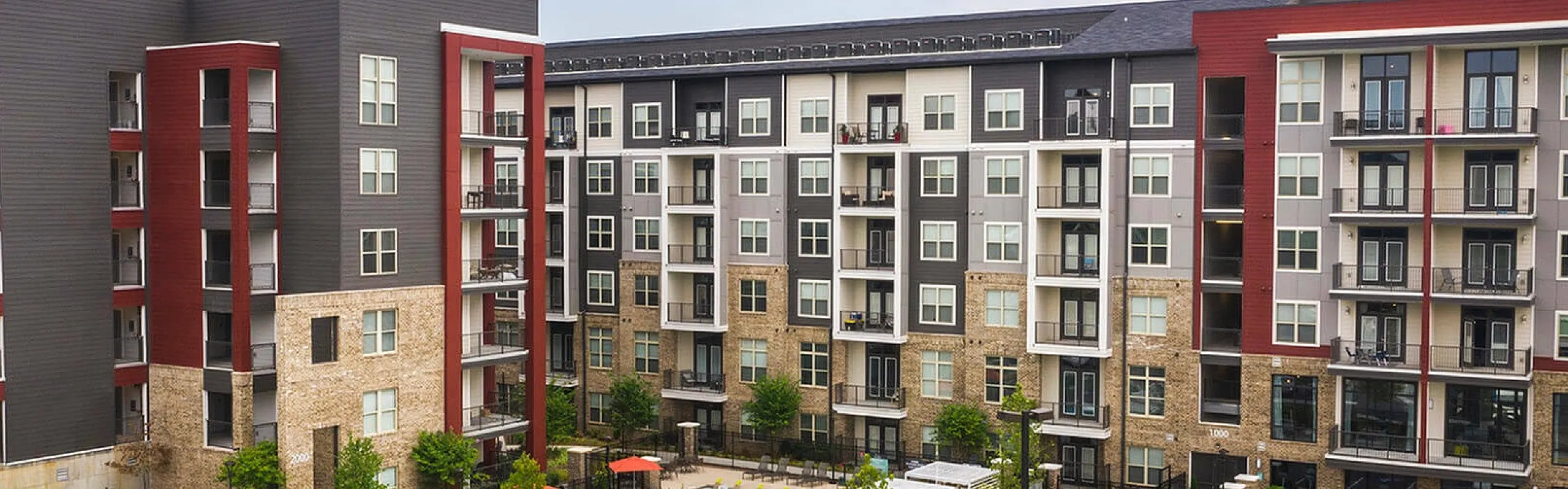 Modern apartment complex with stylish architecture, featuring a vibrant pool area and spacious parking.