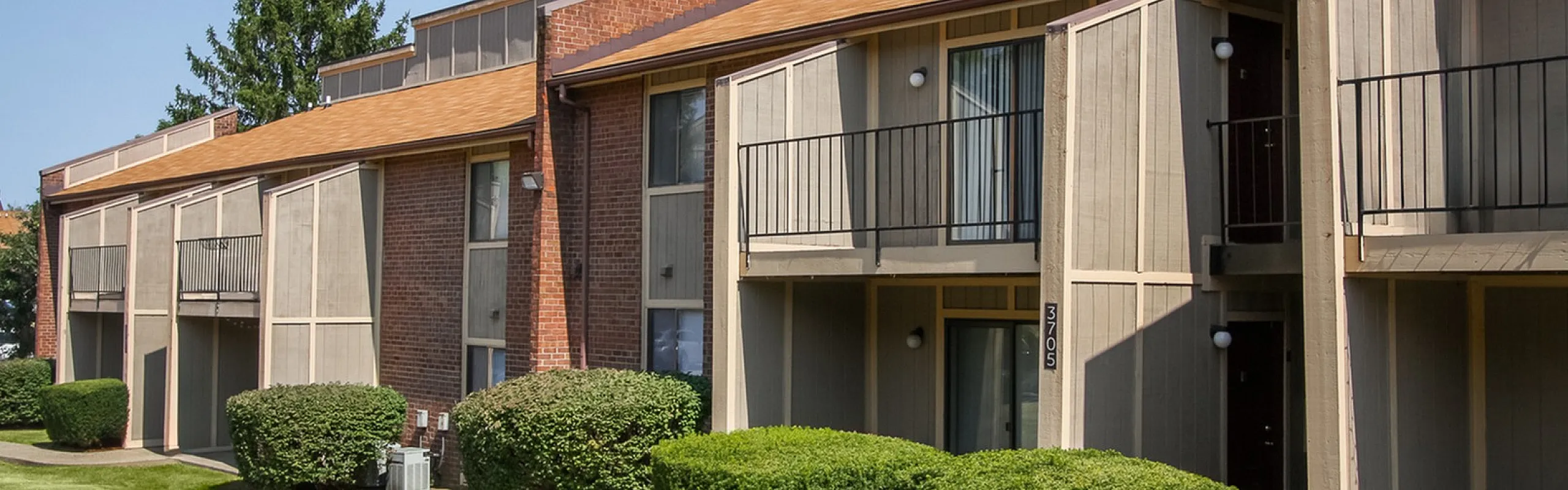 Charming two-story apartment building with modern balconies, surrounded by lush greenery and well-maintained landscaping, offering comfortable living in a serene setting.