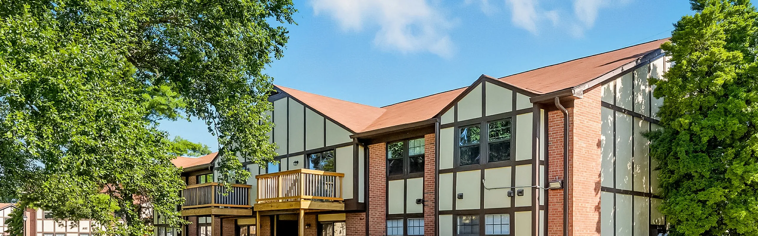Charming apartment building with Tudor-style architecture, surrounded by lush greenery and featuring private balconies.