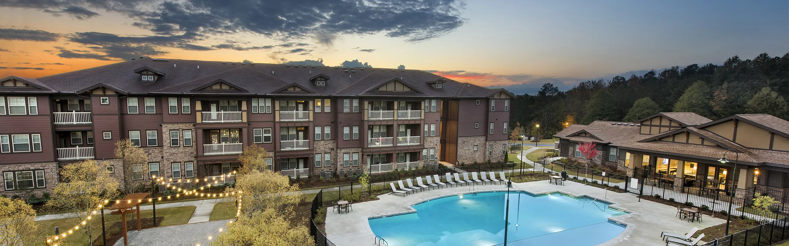 Charming apartment complex at sunset featuring stylish architecture and a luxurious pool with surrounding lounge chairs.