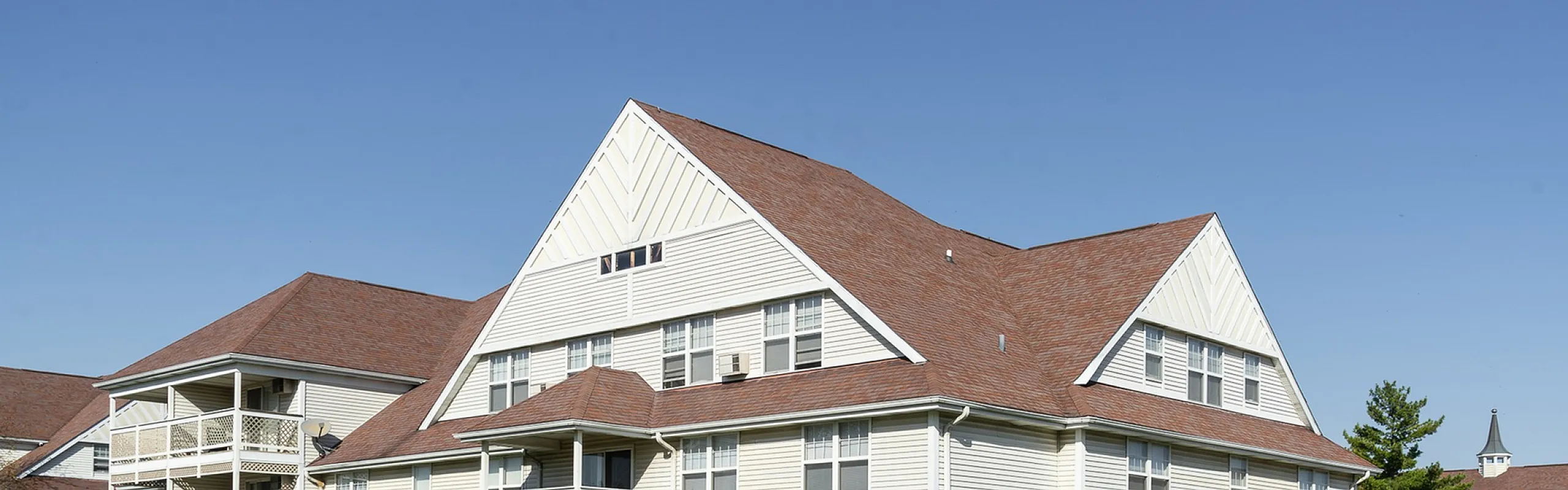 Charming apartment building with a sloped roof and spacious balconies against a clear blue sky.