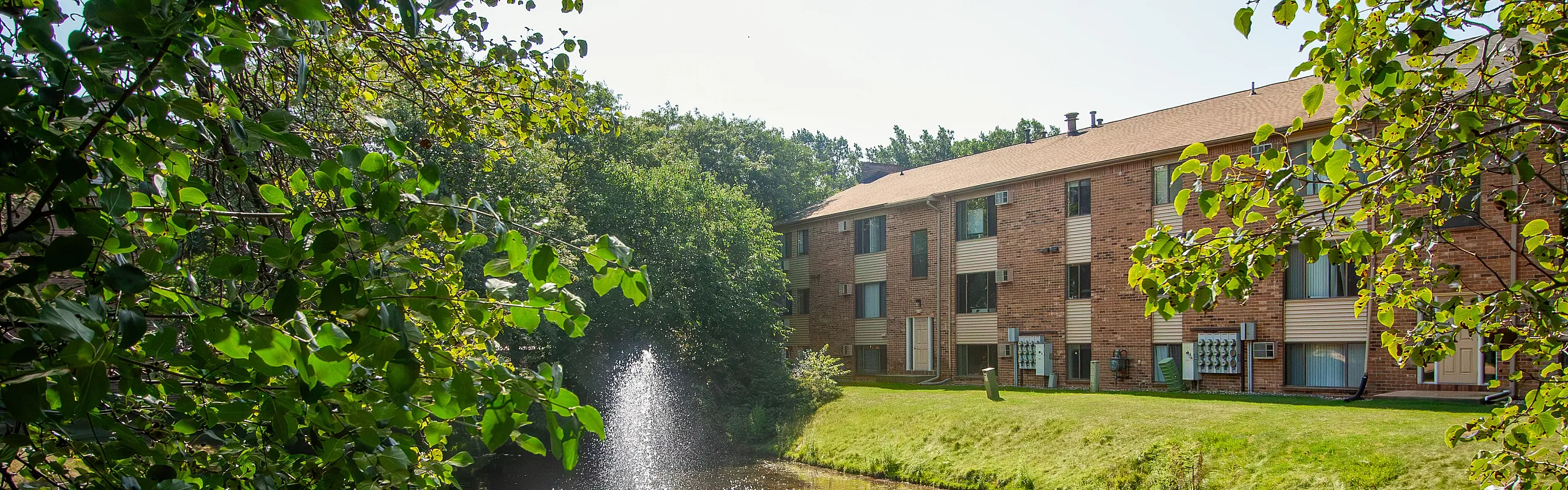 Serene apartment building nestled among lush greenery with a tranquil pond fountain creating a peaceful outdoor environment.