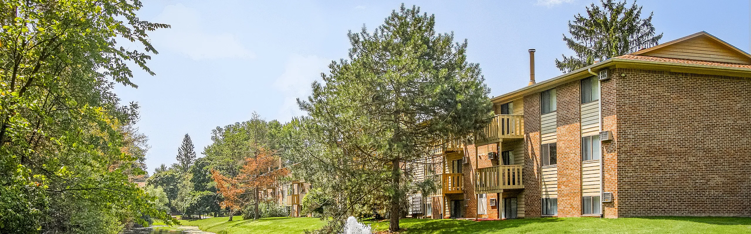 Charming brick apartment building surrounded by lush greenery and serene wooded landscape.
