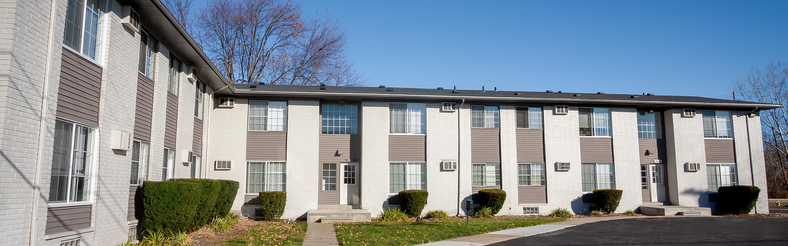 Charming two-story apartment building with modern design, featuring large windows and well-maintained landscaping against a clear blue sky.
