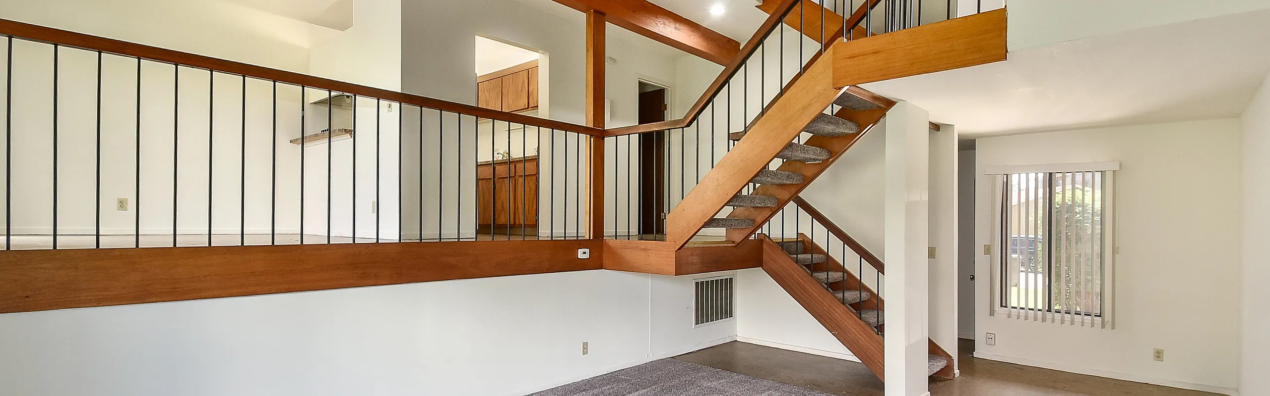 Modern loft-style apartment with open staircase, sleek wooden railing, and large window for natural light.