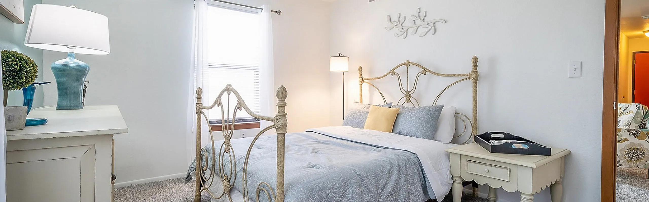 Elegant bedroom with vintage wrought iron bed, soft blue bedding, chic bedside lamps, and natural sunlight creating a tranquil space.