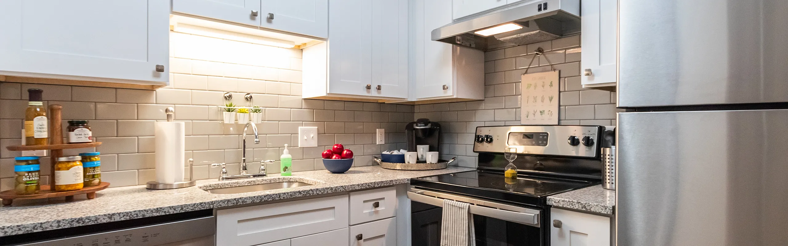 Modern kitchen with sleek stainless steel appliances, granite countertops, and stylish gray tile backsplash.