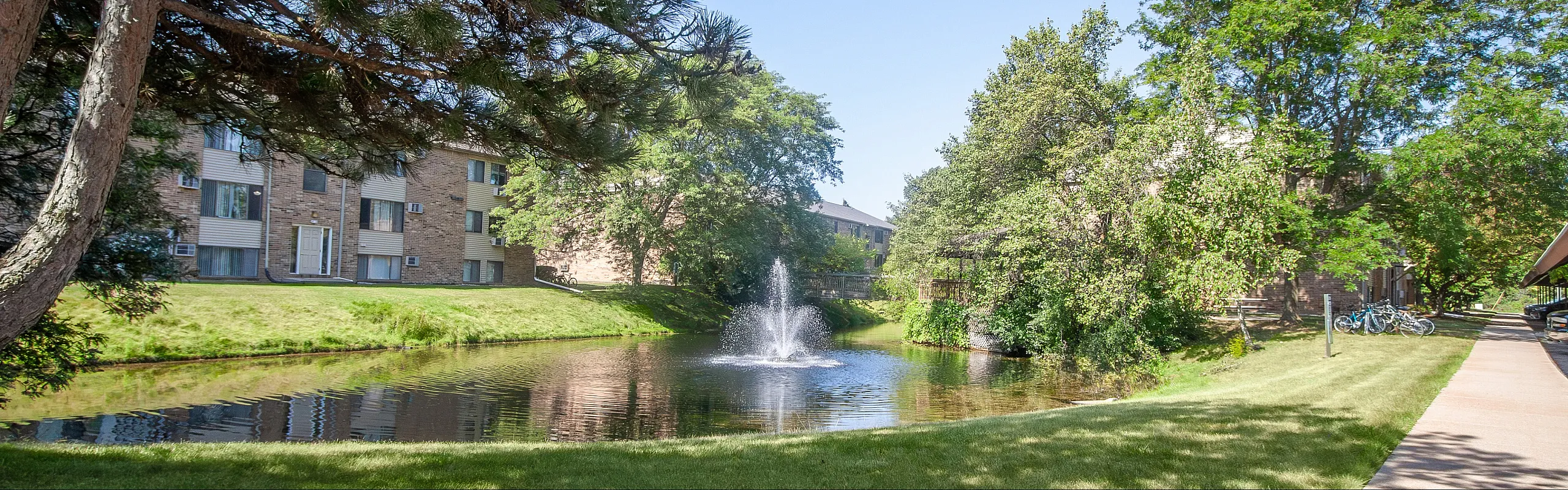 Charming apartment complex with serene pond view, lush greenery, and tranquil fountain, ideal for nature lovers.