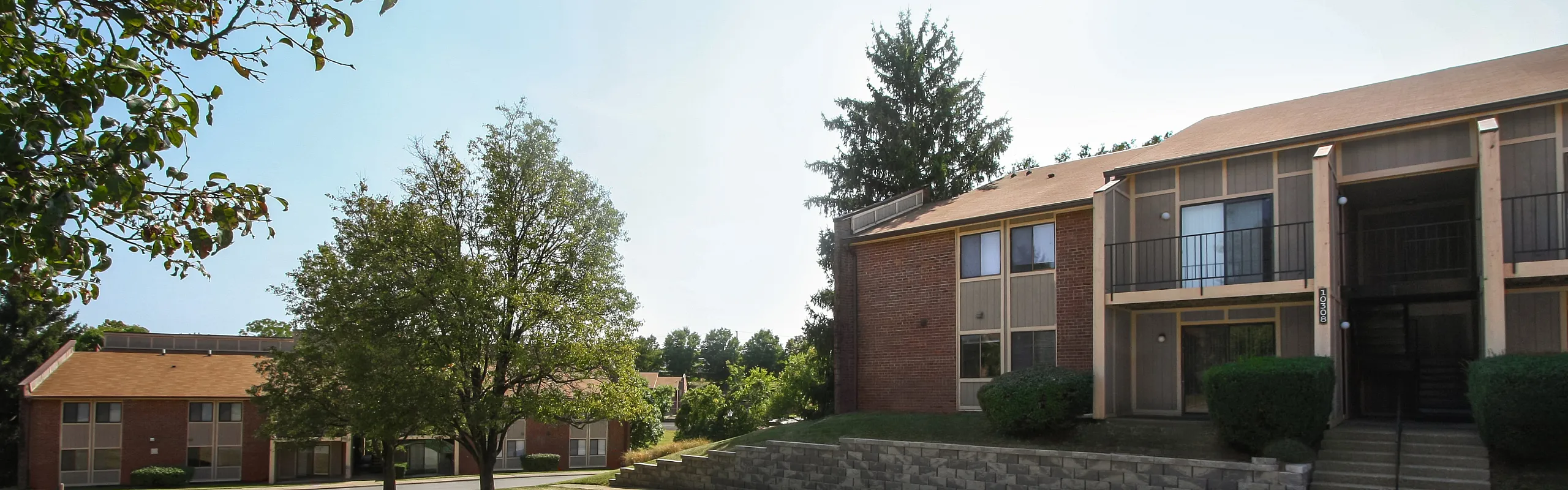 Charming apartment complex with lush greenery and stylish brick facade, offering serene living spaces and community vibes.