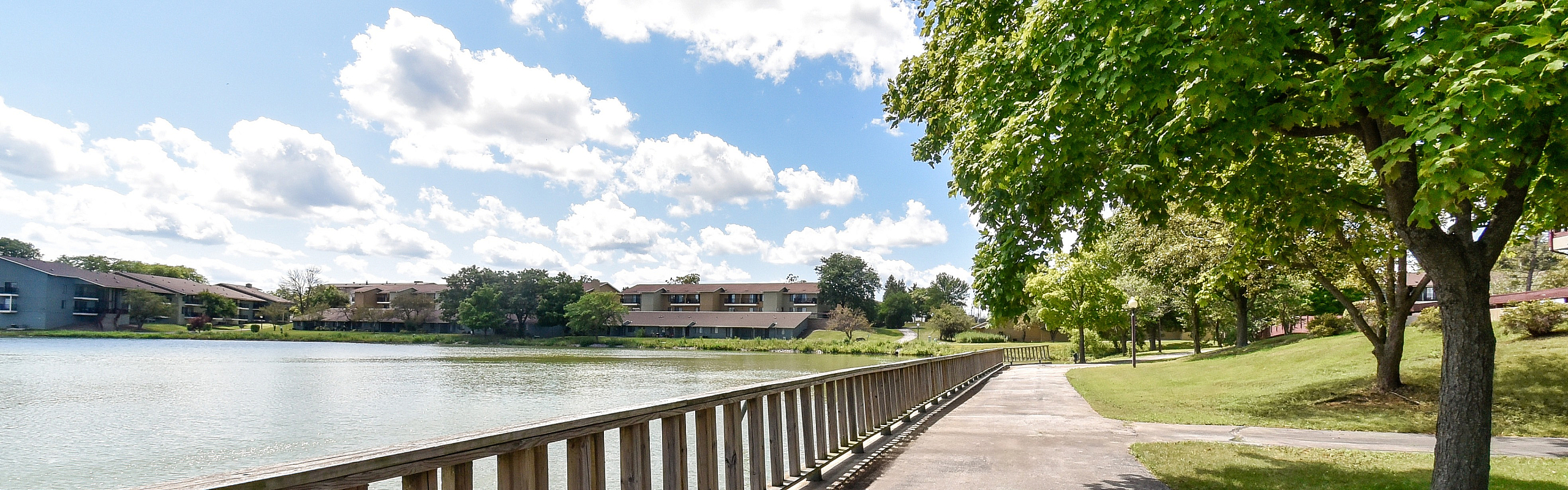 Serene lakeside view showcasing charming apartments surrounded by lush greenery and a scenic walkway.