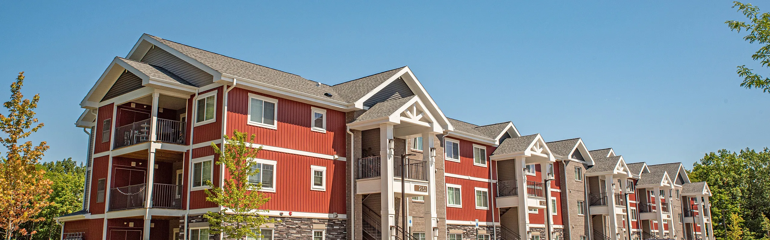 Charming red and white apartment building surrounded by lush greenery, perfect for modern living in a peaceful community.